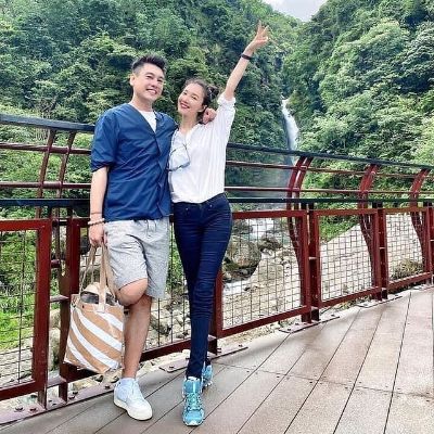 Both are posing on a bridge with waterfall in the background.